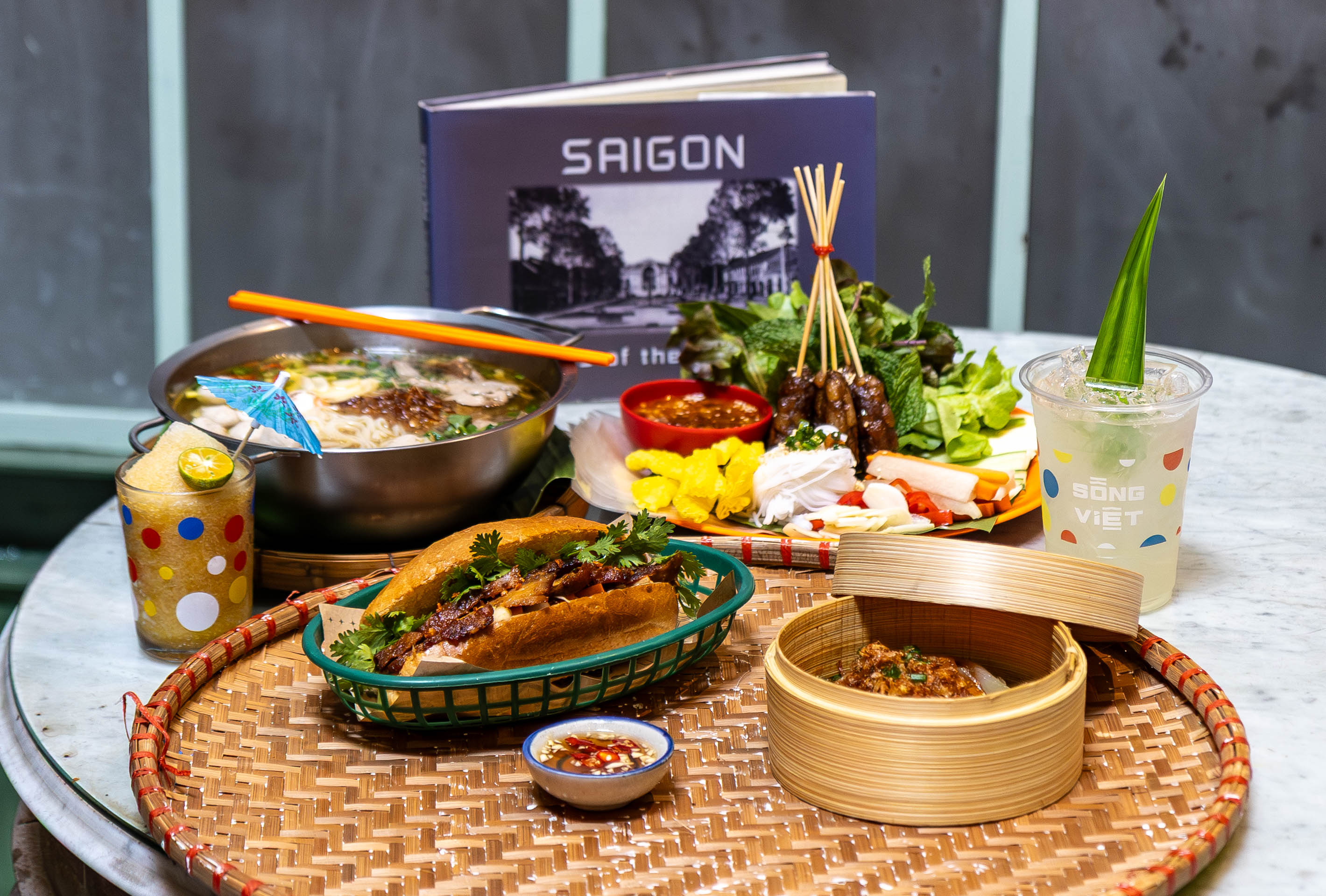 Song Viet at Song Wat signature dishes — Banh Mi, Pho, Nem Nuong, bamboo steamer dim sum and Vietnamese drinks on marble table, Song Wat Road Bangkok